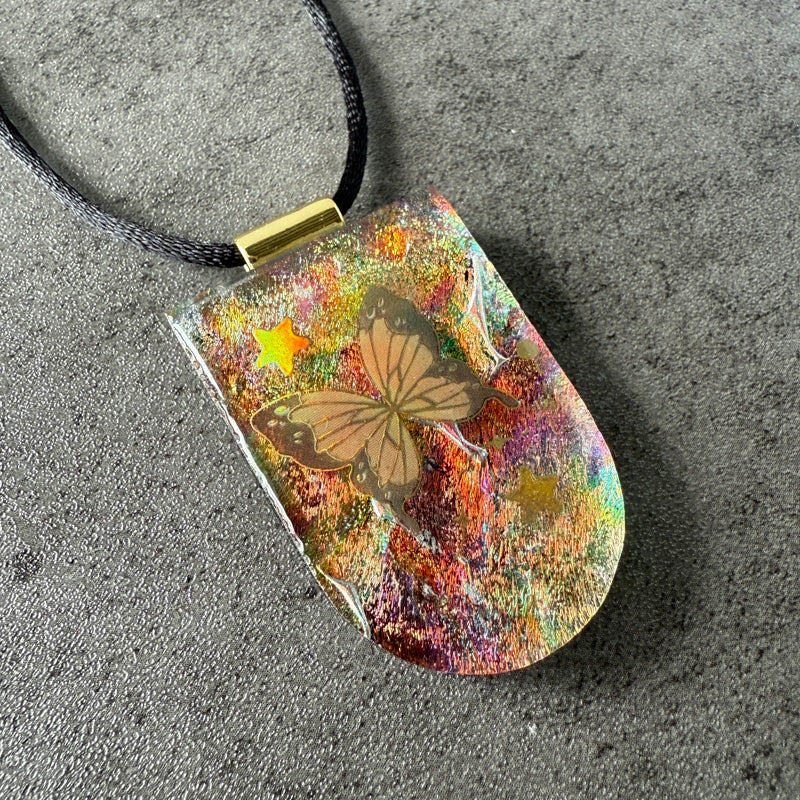 Colorful pendant with butterfly design on a dark surface