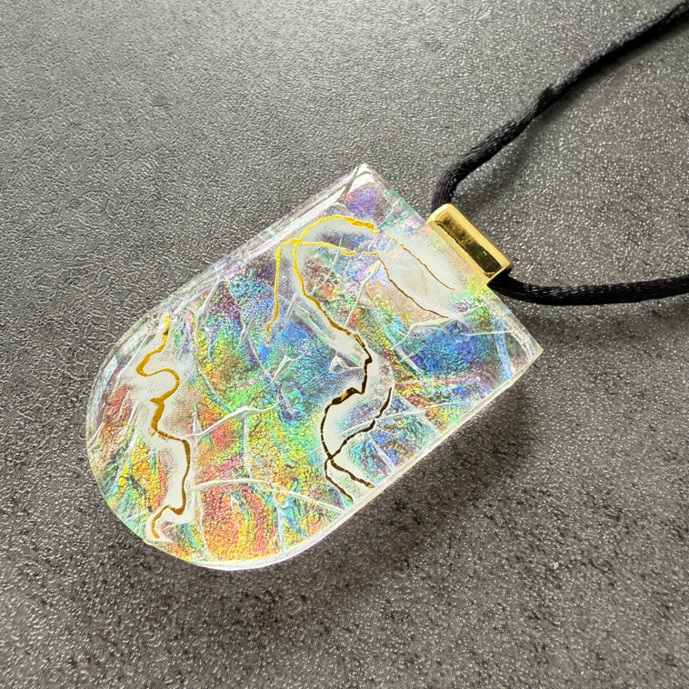 Colorful pendant on a black cord against a gray background