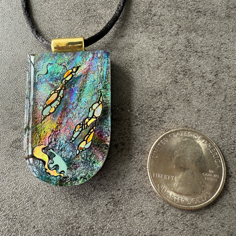 Colorful pendant with butterfly design next to a quarter on a gray surface
