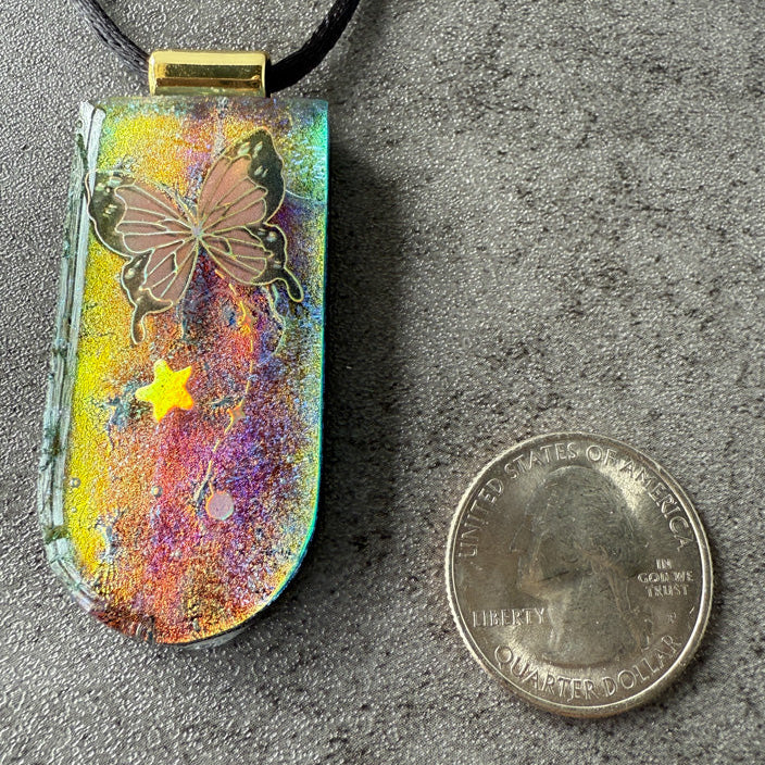 Colorful pendant with butterfly design next to a quarter on a gray surface