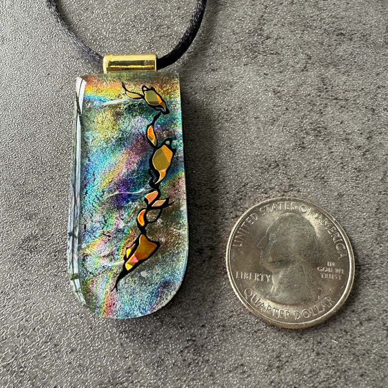Colorful pendant with abstract design next to a quarter on a gray surface
