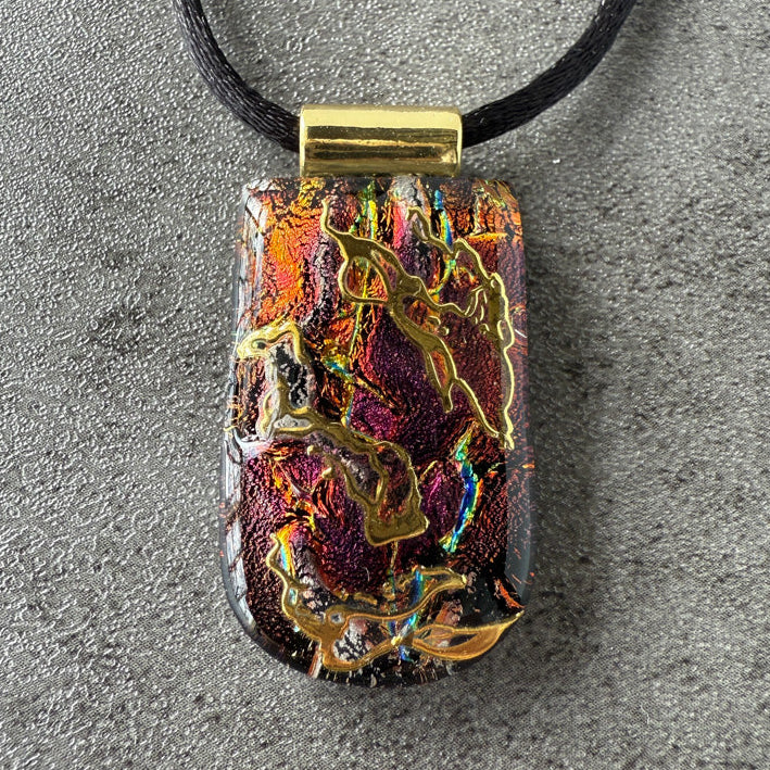 Colorful pendant with gold accents on a black cord against a gray background