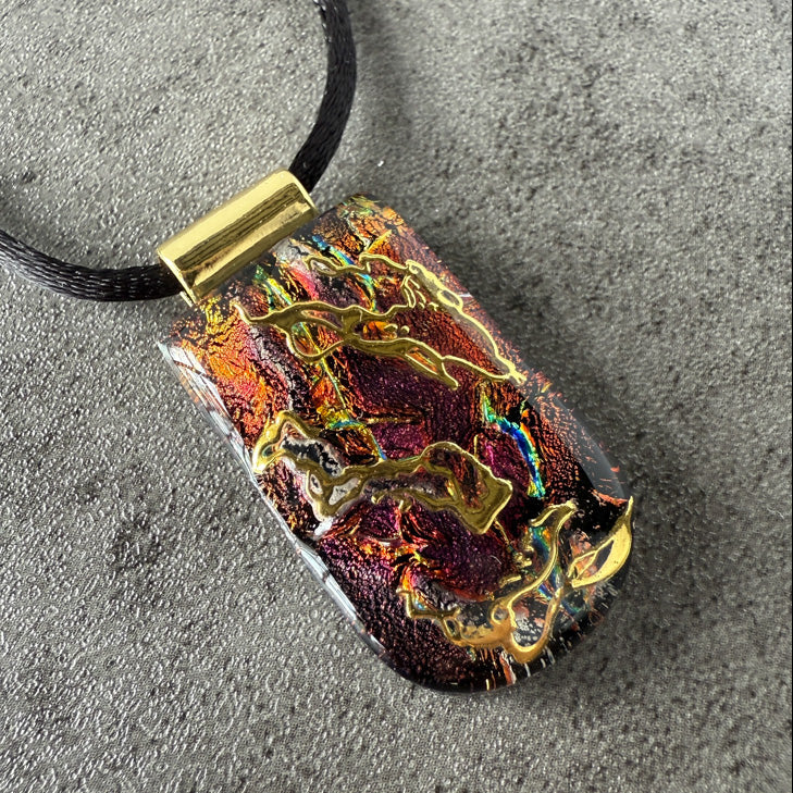 Colorful pendant with gold accents on a black cord against a gray background