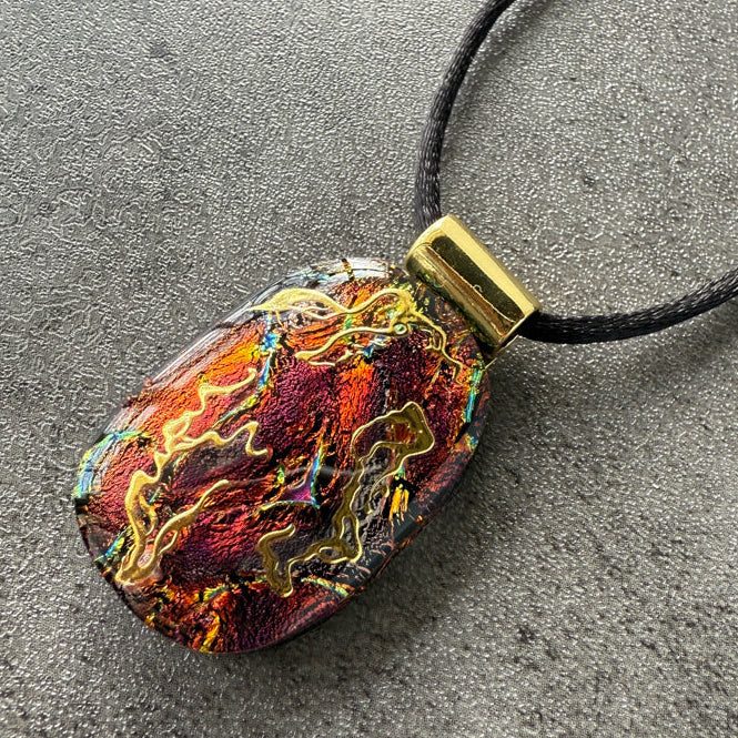 Colorful pendant on a black cord against a gray background