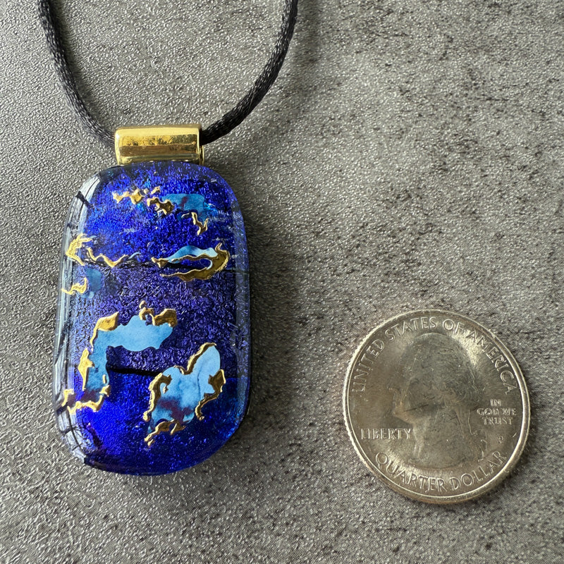Blue pendant with gold accents next to a quarter on a gray surface