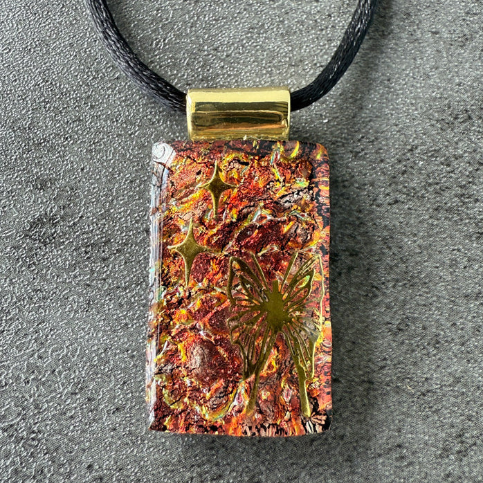 Rectangular pendant with floral design on a black cord against a gray background