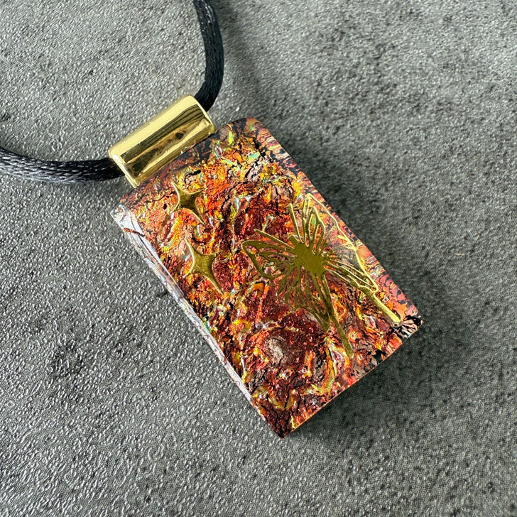 Rectangular pendant with floral design on a black cord against a gray background
