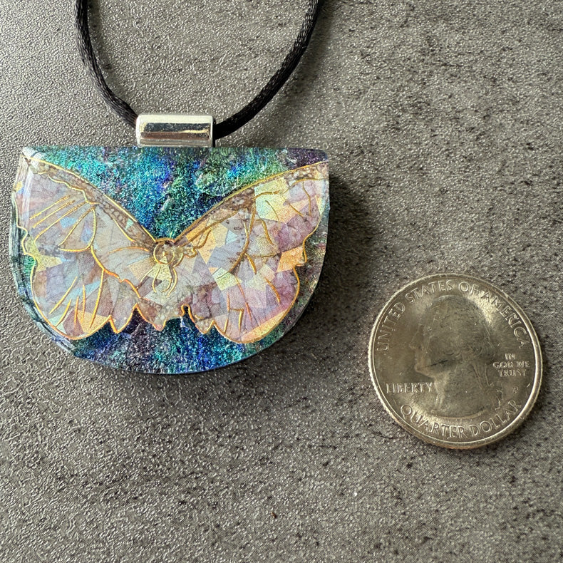 Butterfly-shaped pendant with iridescent finish next to a quarter for scale on a gray surface