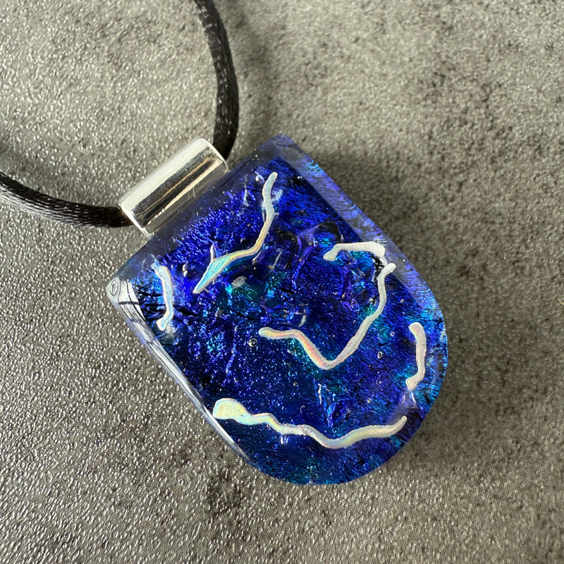 Blue glass pendant with white designs on a gray surface