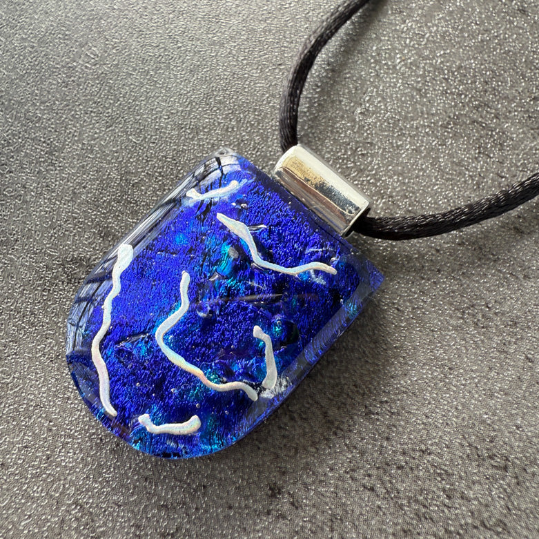 Blue glass pendant with white designs on a black cord against a gray background