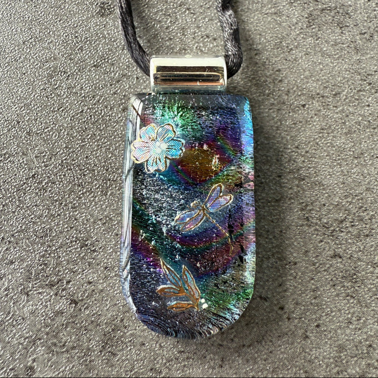 Multicolored pendant with nature-themed designs on a gray surface