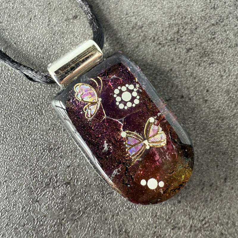 Glass pendant with butterfly design on a textured surface