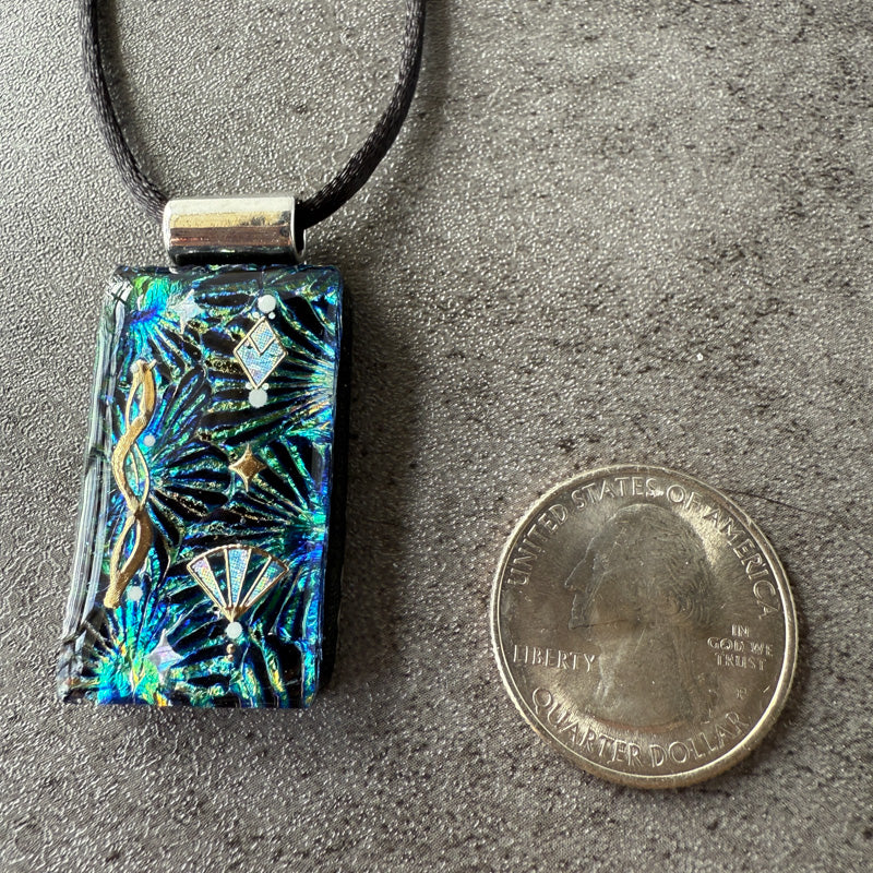 Decorative pendant with tropical leaf design next to a quarter on a gray surface