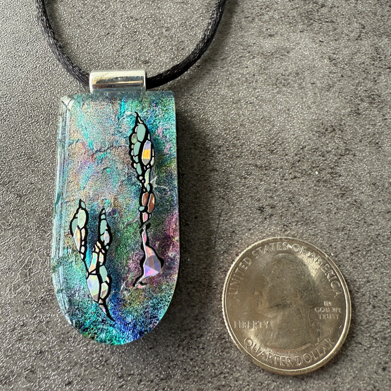 Colorful pendant with abstract design on a gray surface next to a quarter for scale.