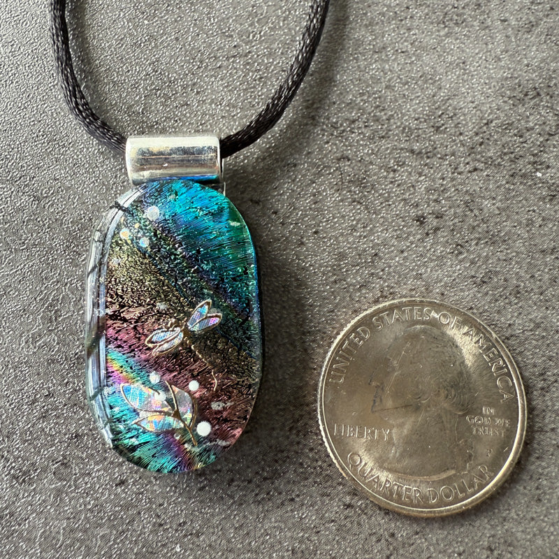 Multicolored pendant on a cord next to a quarter for scale on a gray surface
