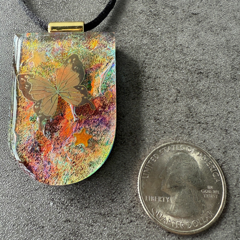 Colorful pendant with butterfly design next to a quarter on a gray surface