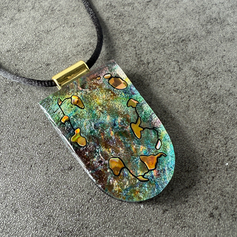 Teardrop-shaped pendant with gold and green design on a gray surface