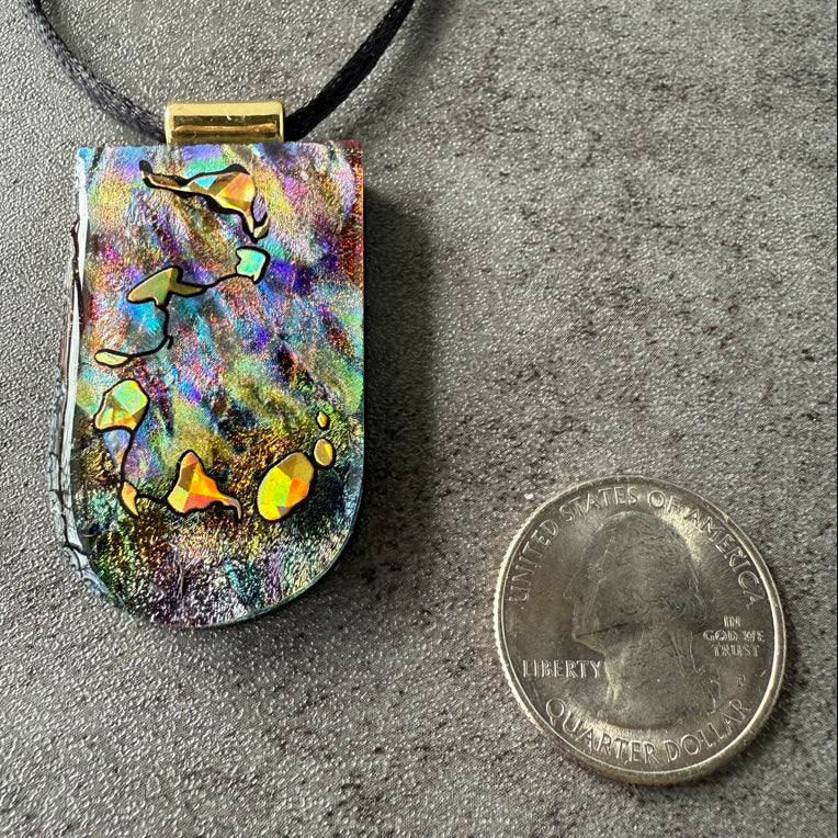 Colorful pendant with abstract design next to a quarter for scale on a gray surface