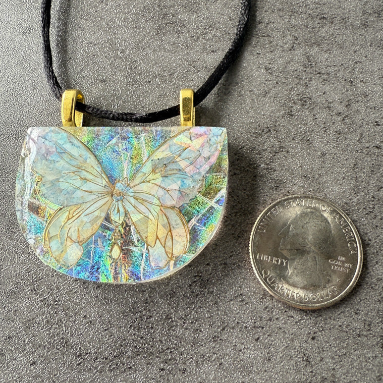 Butterfly-shaped pendant with iridescent wings on a gray surface next to a quarter for scale.