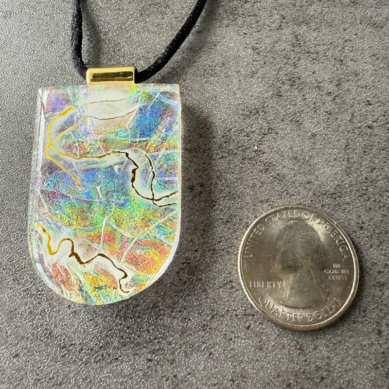 Colorful pendant on a cord next to a quarter for scale on a gray surface