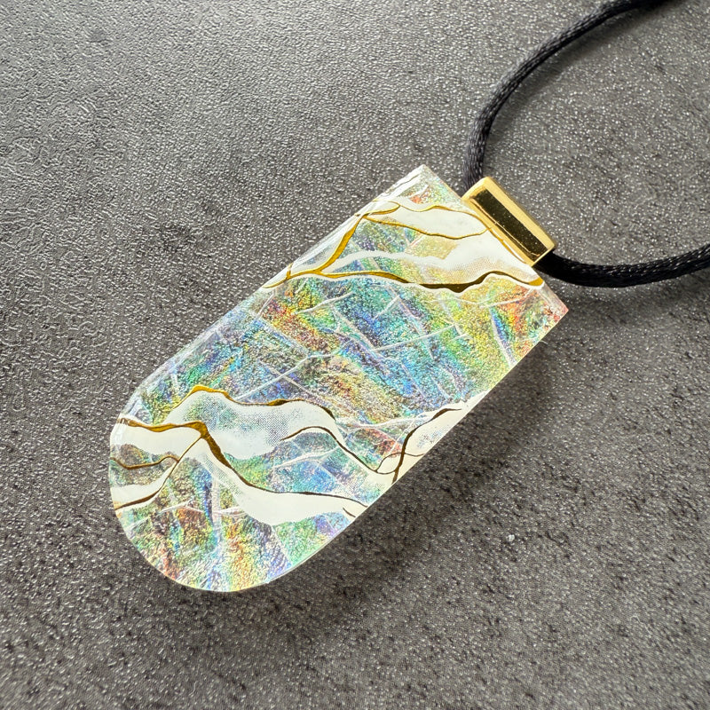Iridescent pendant with gold accents on a black cord against a gray background