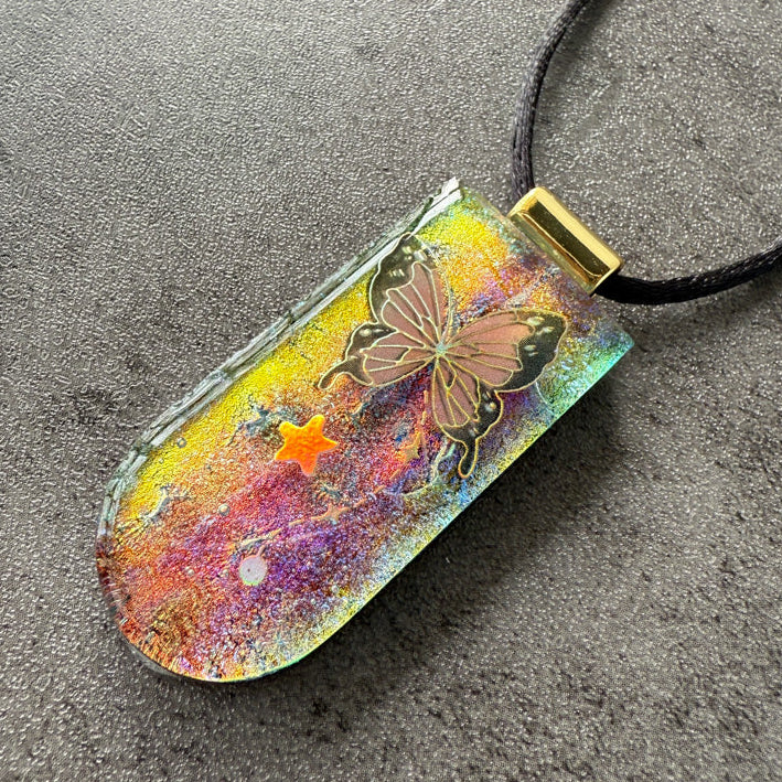 Colorful pendant with butterfly design on a dark surface