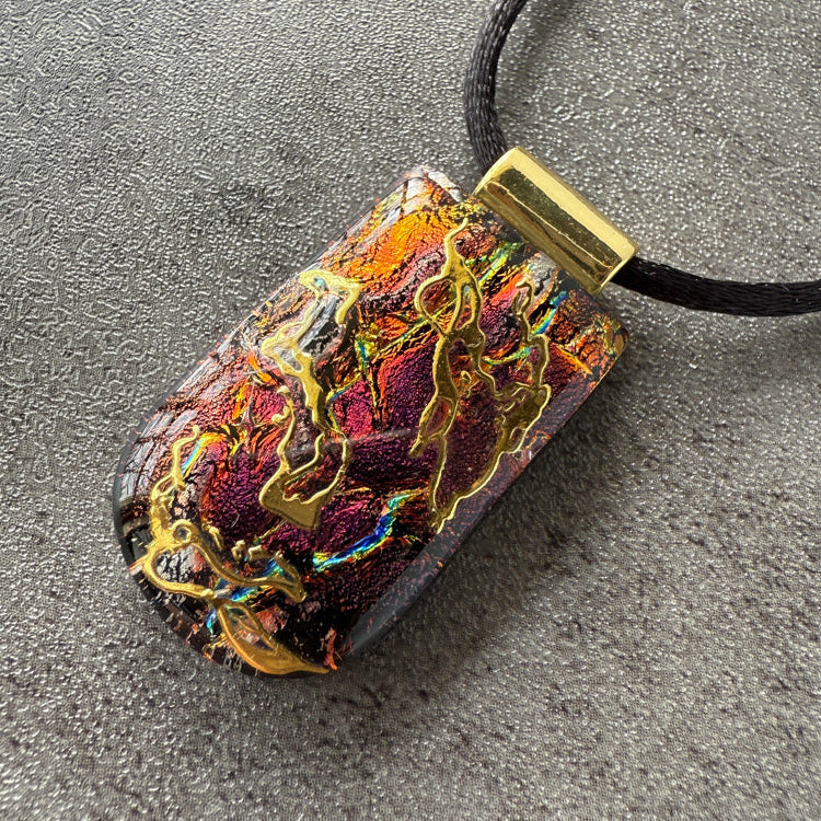 Colorful pendant with gold accents on a black cord against a gray background
