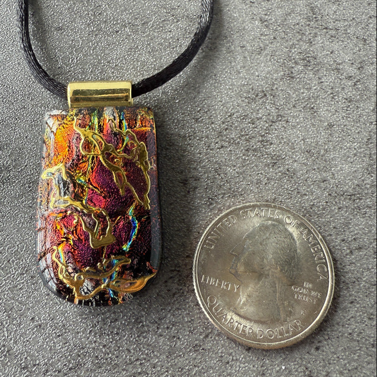 Colorful pendant on a black cord next to a quarter for scale on a gray surface
