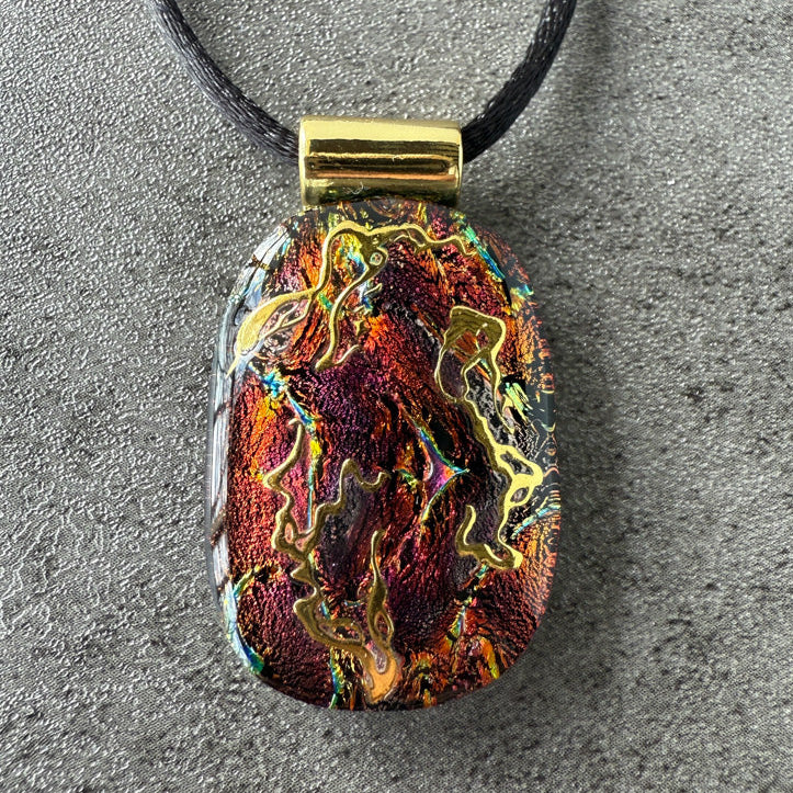 Multicolored pendant on a black cord against a gray background