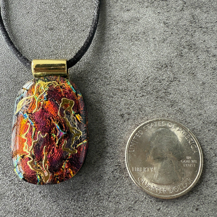 Colorful pendant on a black cord next to a quarter for scale on a gray surface