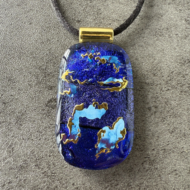 Blue pendant with gold accents on a gray surface