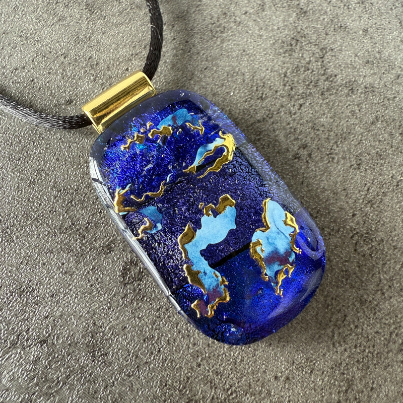 Blue pendant with gold accents on a gray surface