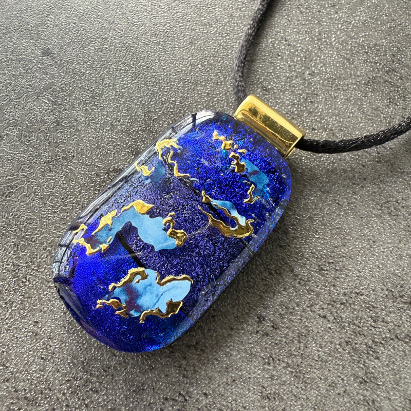 Blue pendant with gold accents on a dark gray surface