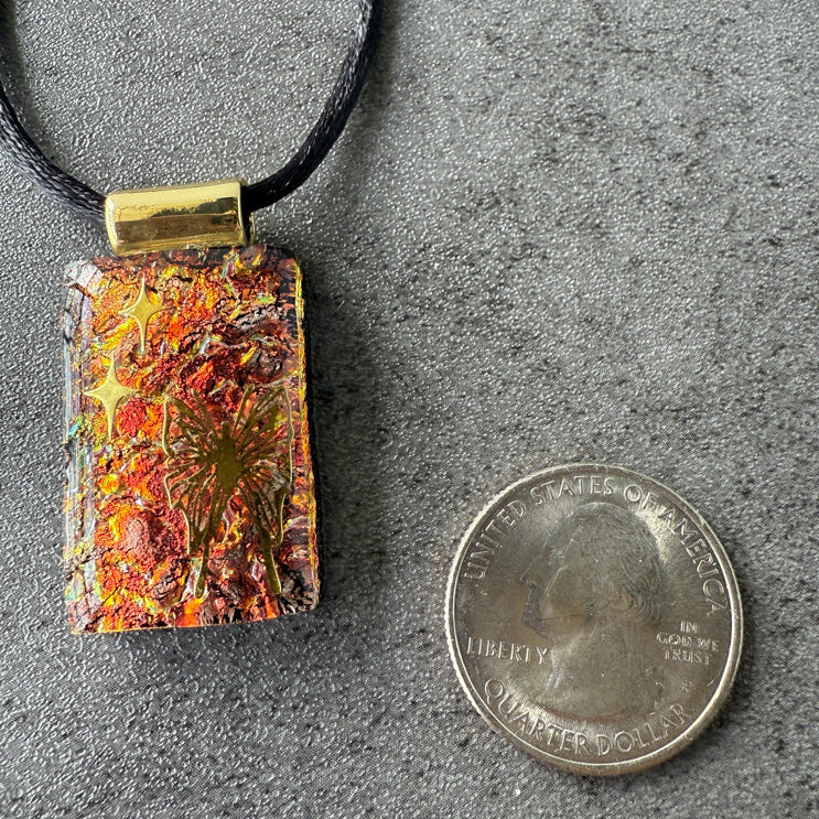Rectangular pendant with a star design on a black cord, next to a quarter for scale, on a gray surface.