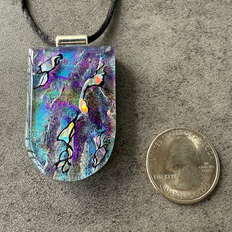 Colorful pendant with abstract design on a gray surface next to a quarter for scale.