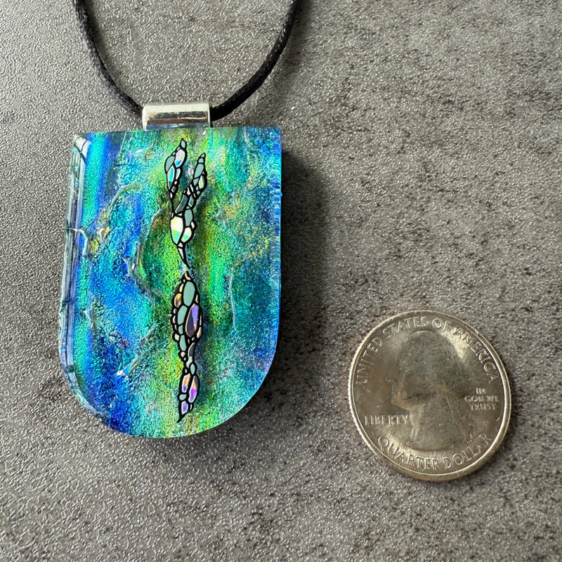 Colorful pendant on a cord next to a quarter for scale on a gray surface
