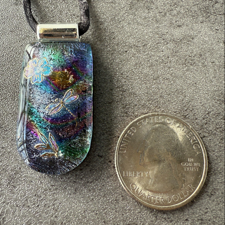 Multicolored pendant with butterfly designs next to a quarter on a gray surface