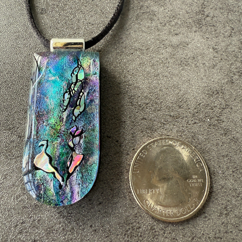 Colorful pendant with bird design next to a quarter on a gray surface
