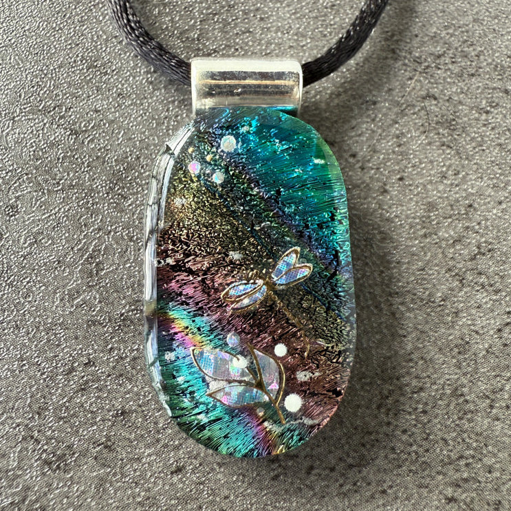 Multicolored pendant with dragonfly design on a gray surface